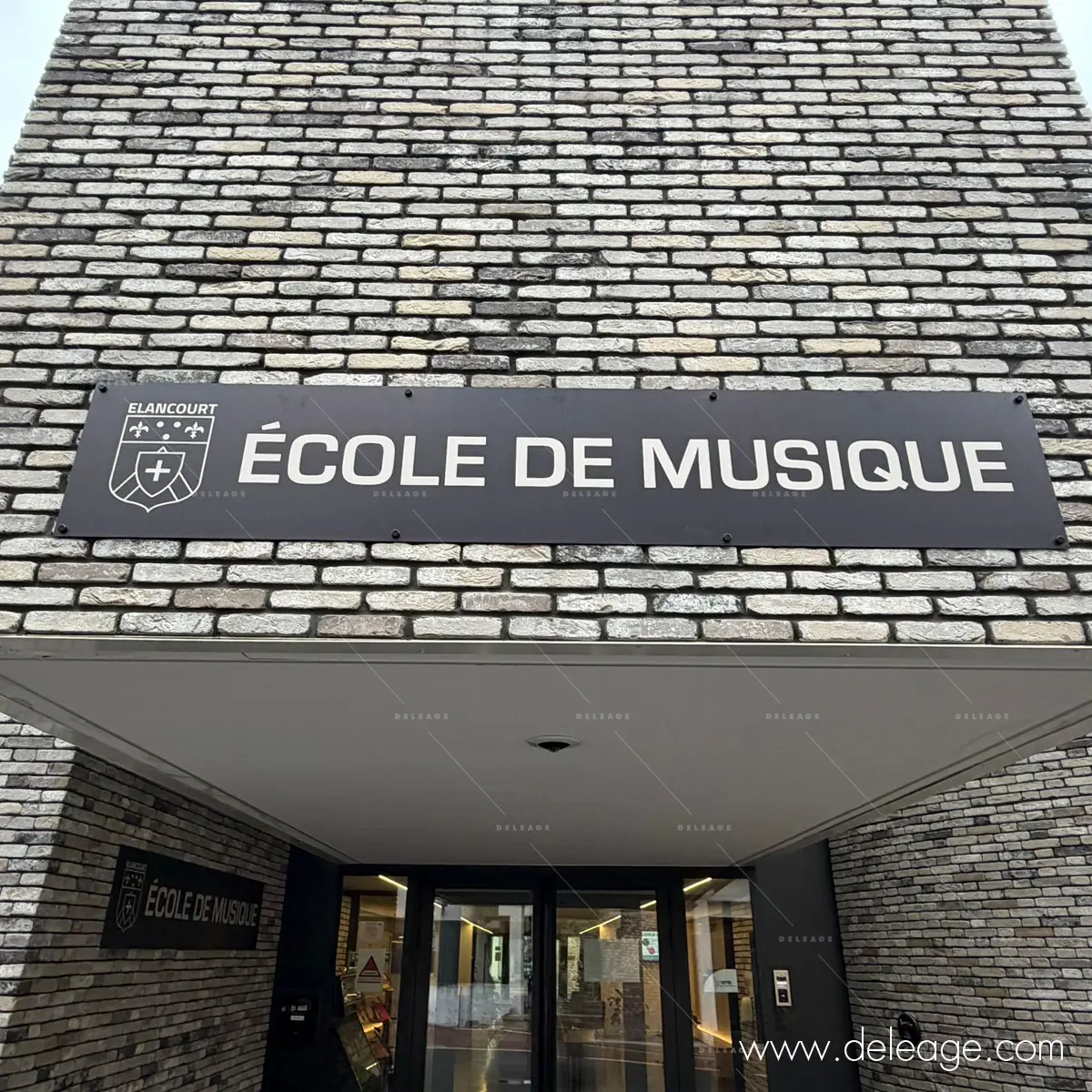 1-enseigne-en-relief-elancourt Enseigne en relief avec logo et lettrage blanc sur fond noir à l'entrée de l'école.